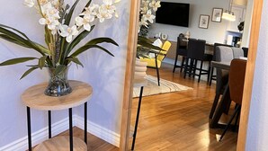 A living room with a wooden floor, a round table with a vase of flowers, and a large mirror reflecting the room. - 🏡 Joyful Vacation Home 🏡  (Anaheim)