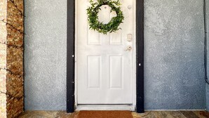 A white door with a wreath, a brown doormat with text, and a stone wall to the left. - 🏡 Joyful Vacation Home 🏡  (Anaheim)