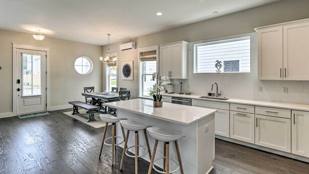 A modern kitchen with white cabinetry, a central island with stools, and a dining area with a bench. - Inlet Beach Cottage: Close to Beach Access! (Inlet Beach)