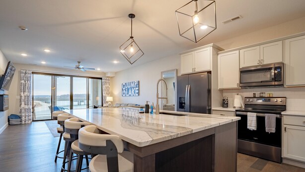 A modern kitchen with a large island, bar stools, stainless steel appliances, and a view to the outside.
