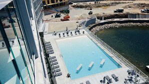 A rooftop pool with sun loungers and a view of a construction site.
