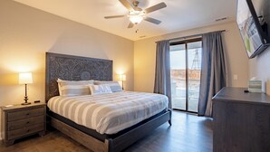 A bedroom with a bed, nightstands, a ceiling fan, a TV, and a view of the outdoors.