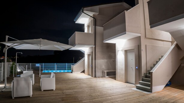 Una terraza moderna al aire libre con muebles de mimbre blanco y sombrillas, una escalera y un área de piscina al fondo.