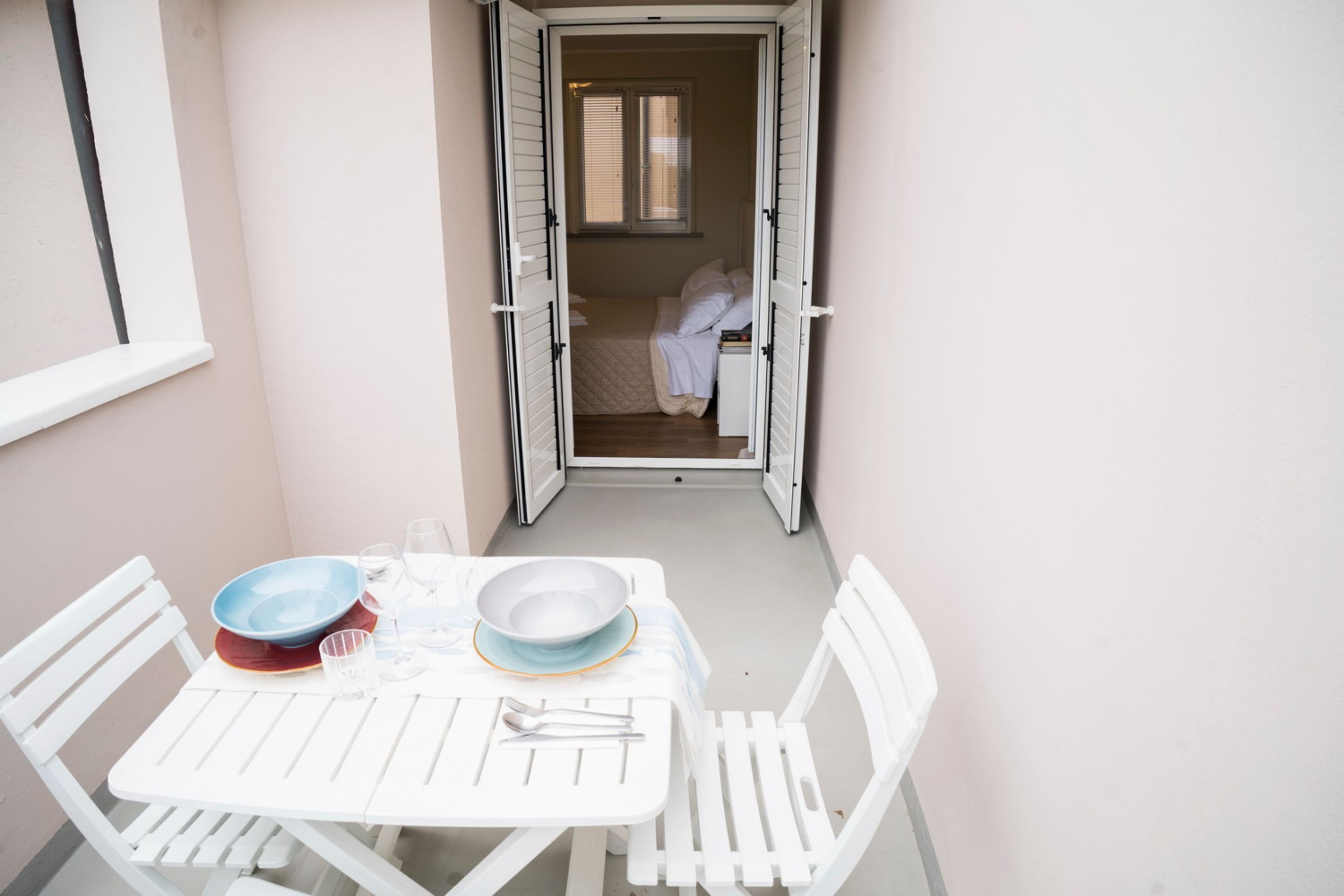 Una habitación pequeña y de diseño abierto con una cama y una ventana. Hay una mesa blanca con algunos objetos encima, y una silla blanca.