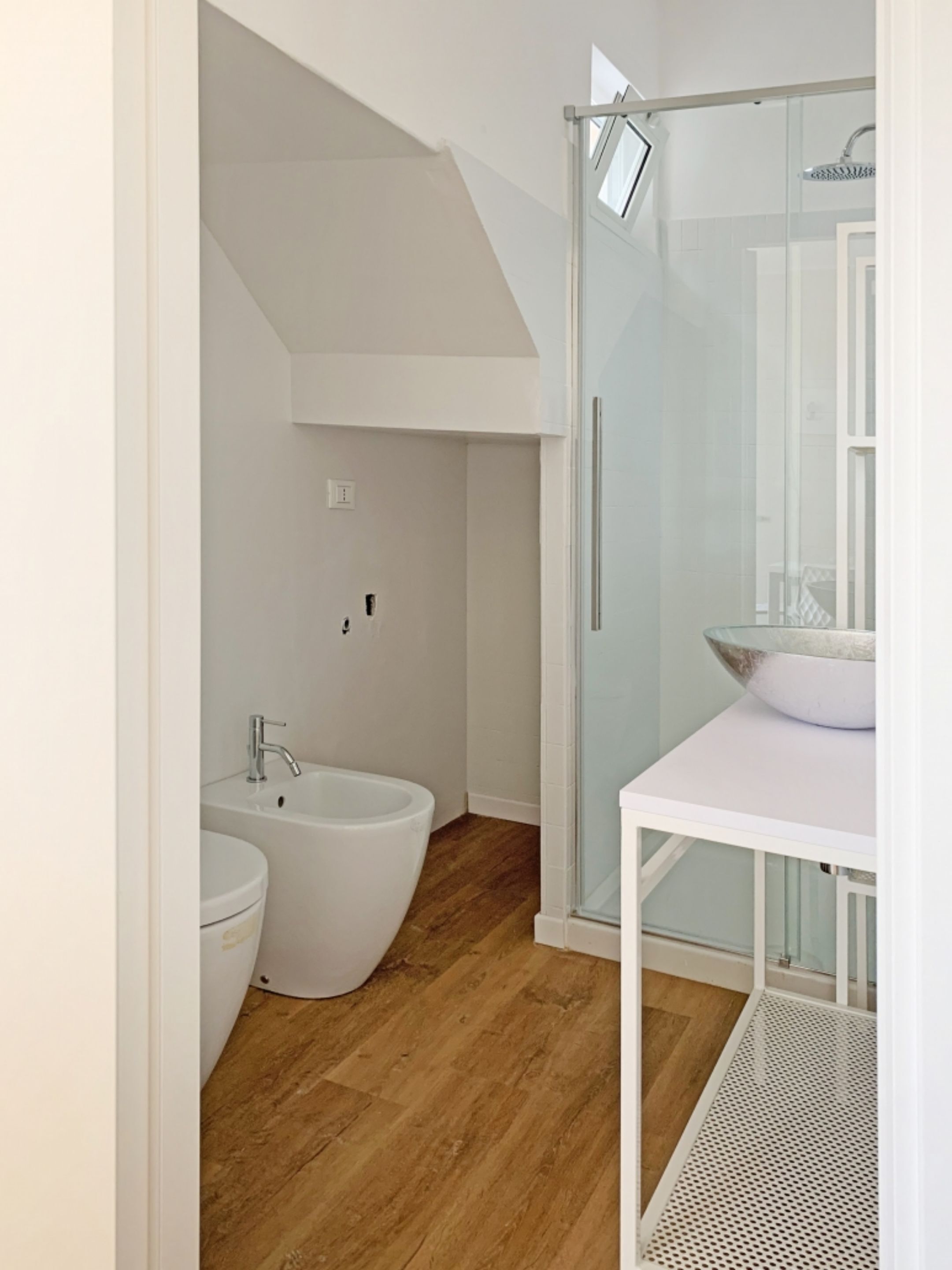 A modern bathroom with a glass shower enclosure, a white sink, and a bidet.