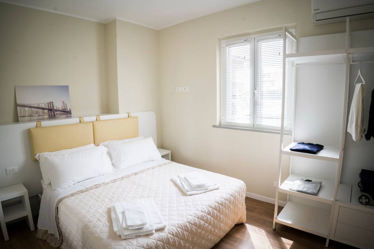 Une chambre bien rangée, avec un lit, une table de chevet, une armoire et une fenêtre équipée de stores.