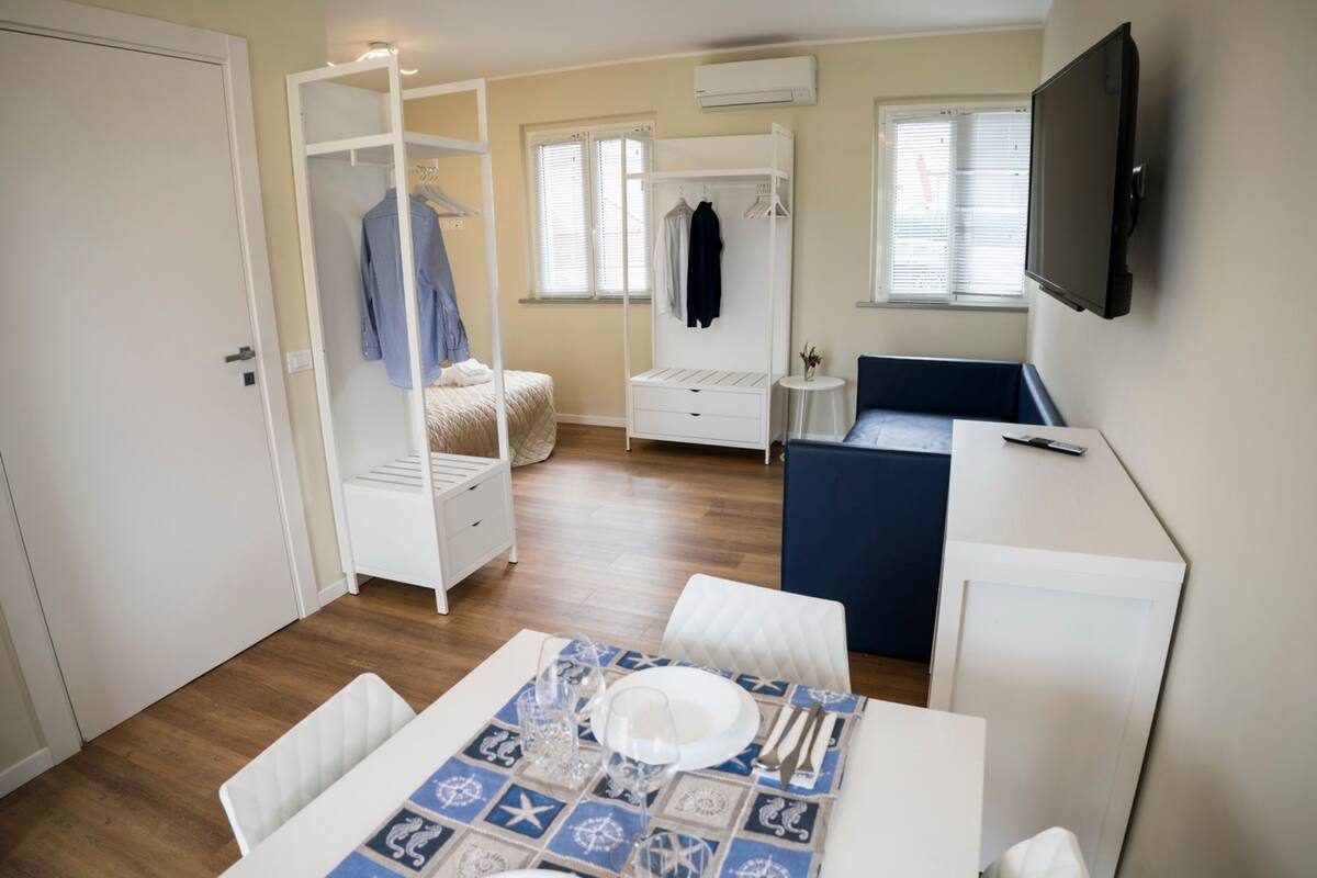 Une pièce de taille modeste comprenant un lit, un bureau, une chaise, une table dressée pour le repas et un téléviseur fixé au mur.