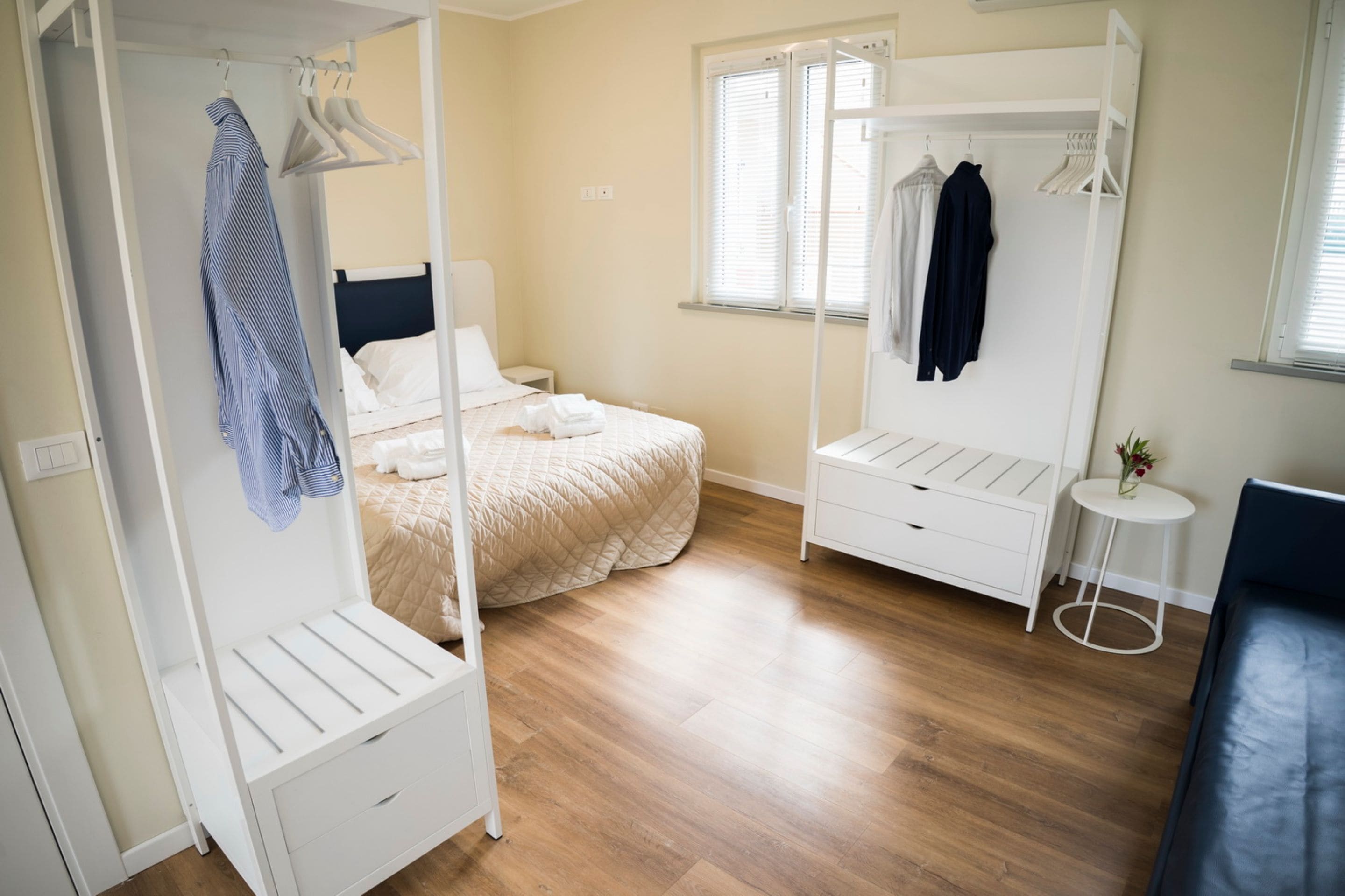 A bedroom with a bed, a wardrobe, a small table, and a window.