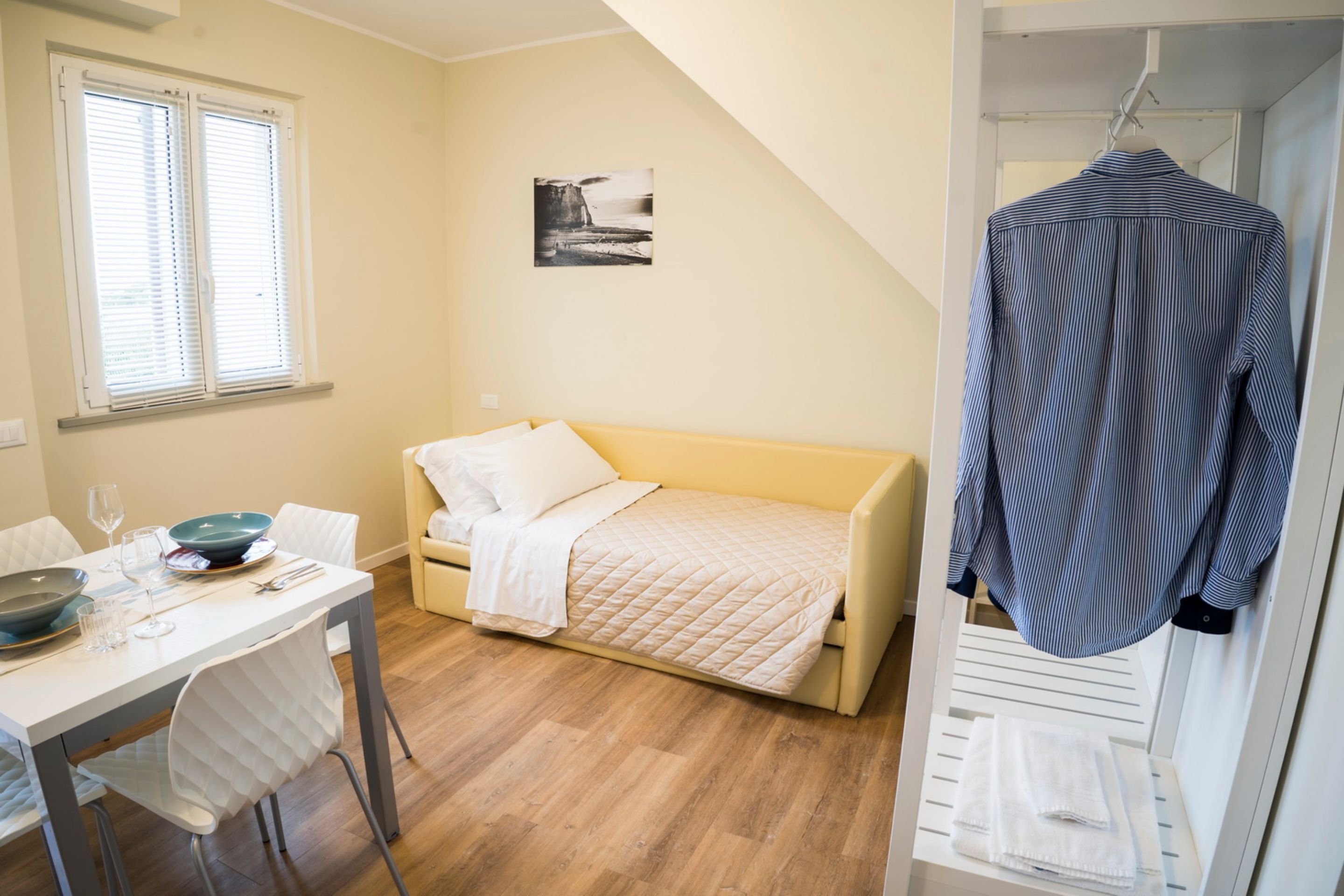 Ein kleiner, gut beleuchteter Raum mit einem Bett, einem Esstisch mit Stühlen und einem Hängemantel.