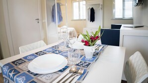 Una mesa de comedor dispuesta con platos, vasos y cubiertos, una jarra blanca con flores y un camino de mesa estampado.
