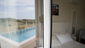 Un dormitorio con una cama grande, vista a una piscina y una puerta que da a otra habitación.