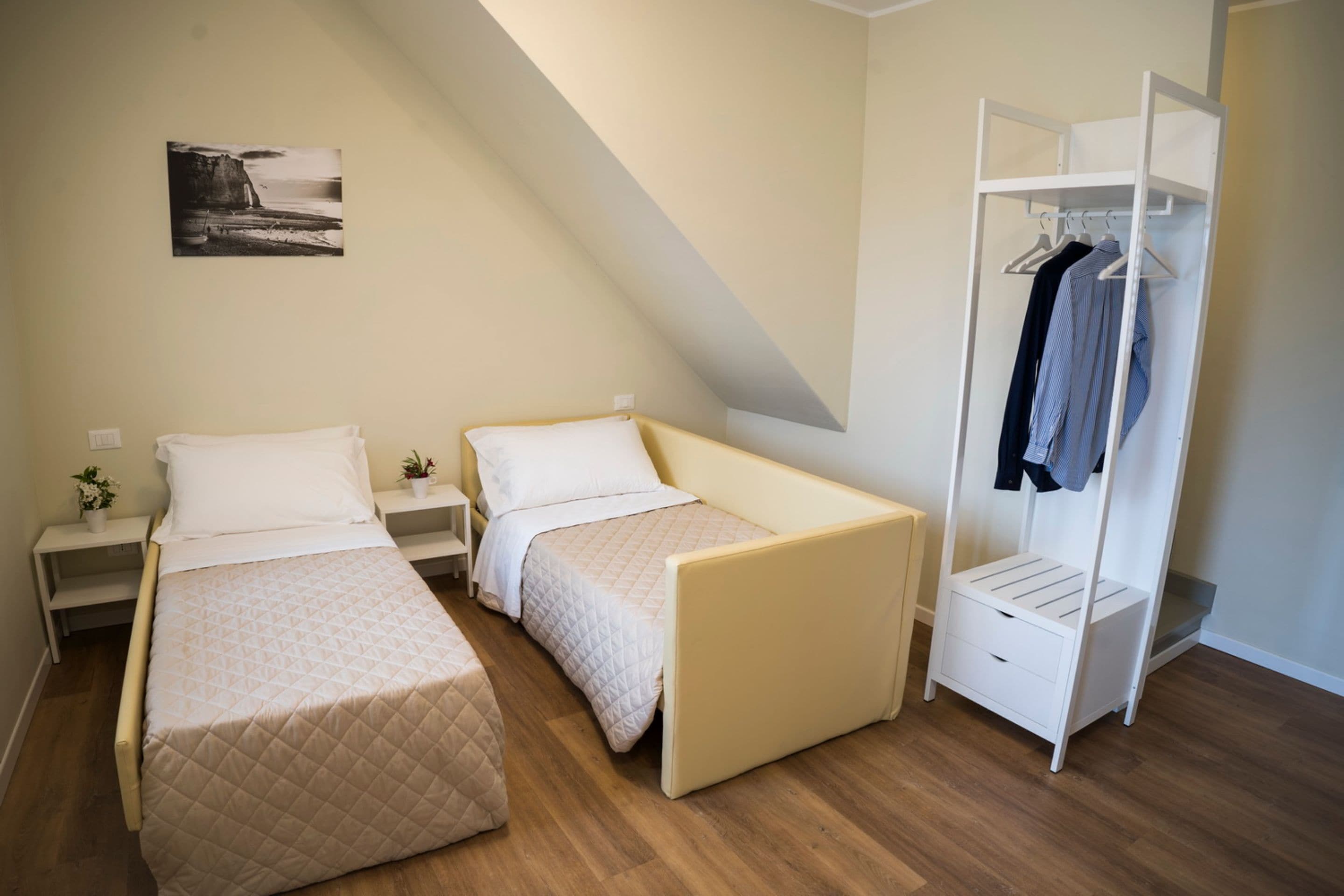 A bedroom with two beds, a wardrobe, and a bedside table with a plant.