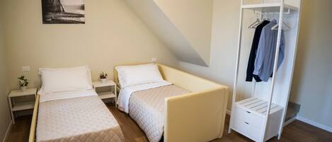 A bedroom with two beds, a wardrobe, and a bedside table with a plant.