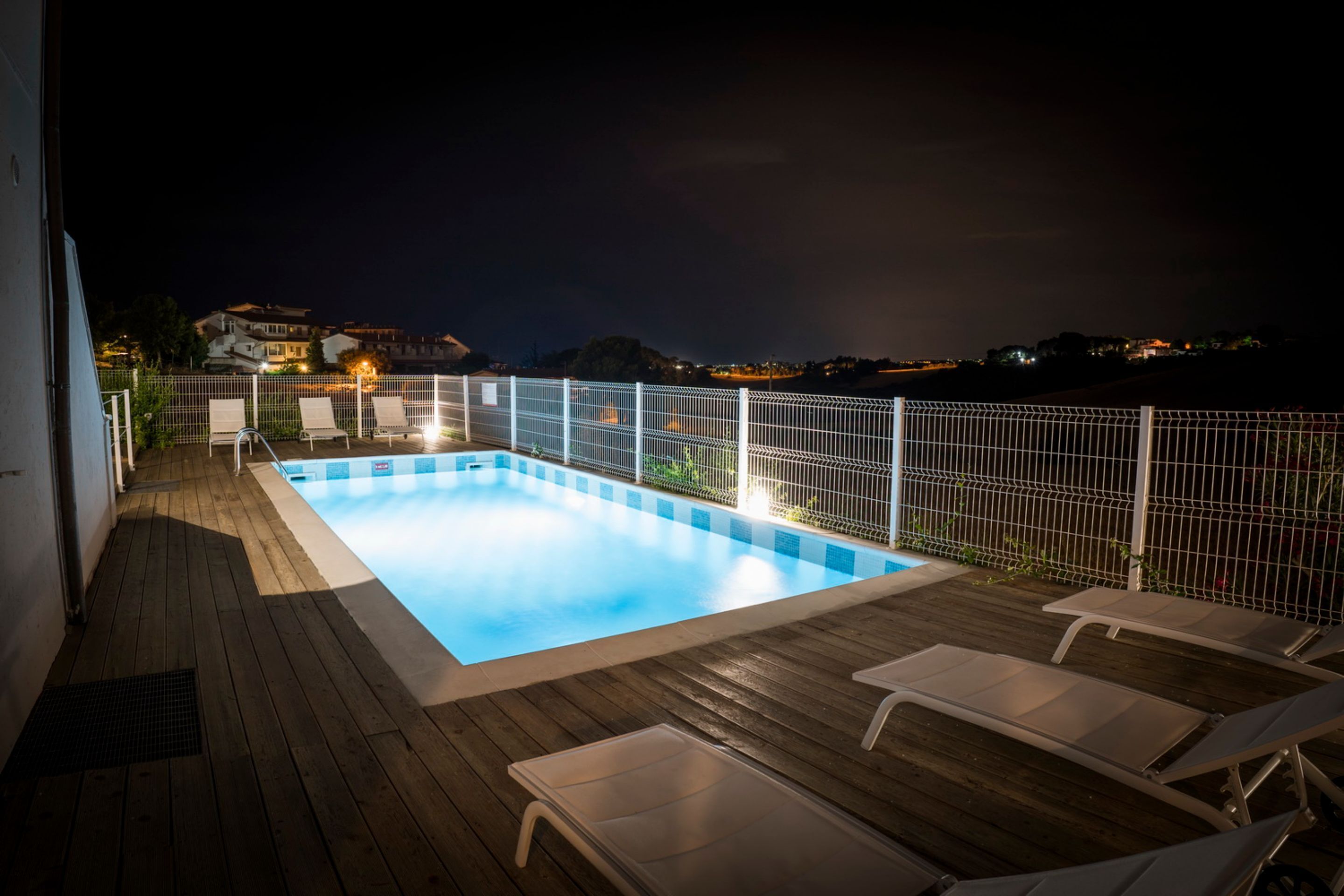 Ein Schwimmbecken mit Holzterrasse, Liegestühlen und einem weißen Zaun.