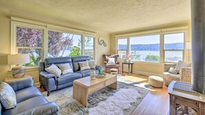 A spacious living room with a fireplace, large windows, and a view of the outdoors. - Direct Beach Access: Getaway on Port Orchard! (Bremerton)
