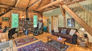 A spacious loft with exposed wooden beams, a cozy living area with a couch and bookshelves, a massage chair, and a staircase. - Pet-Friendly Leicester/Asheville Mtn View Escape (Leicester)