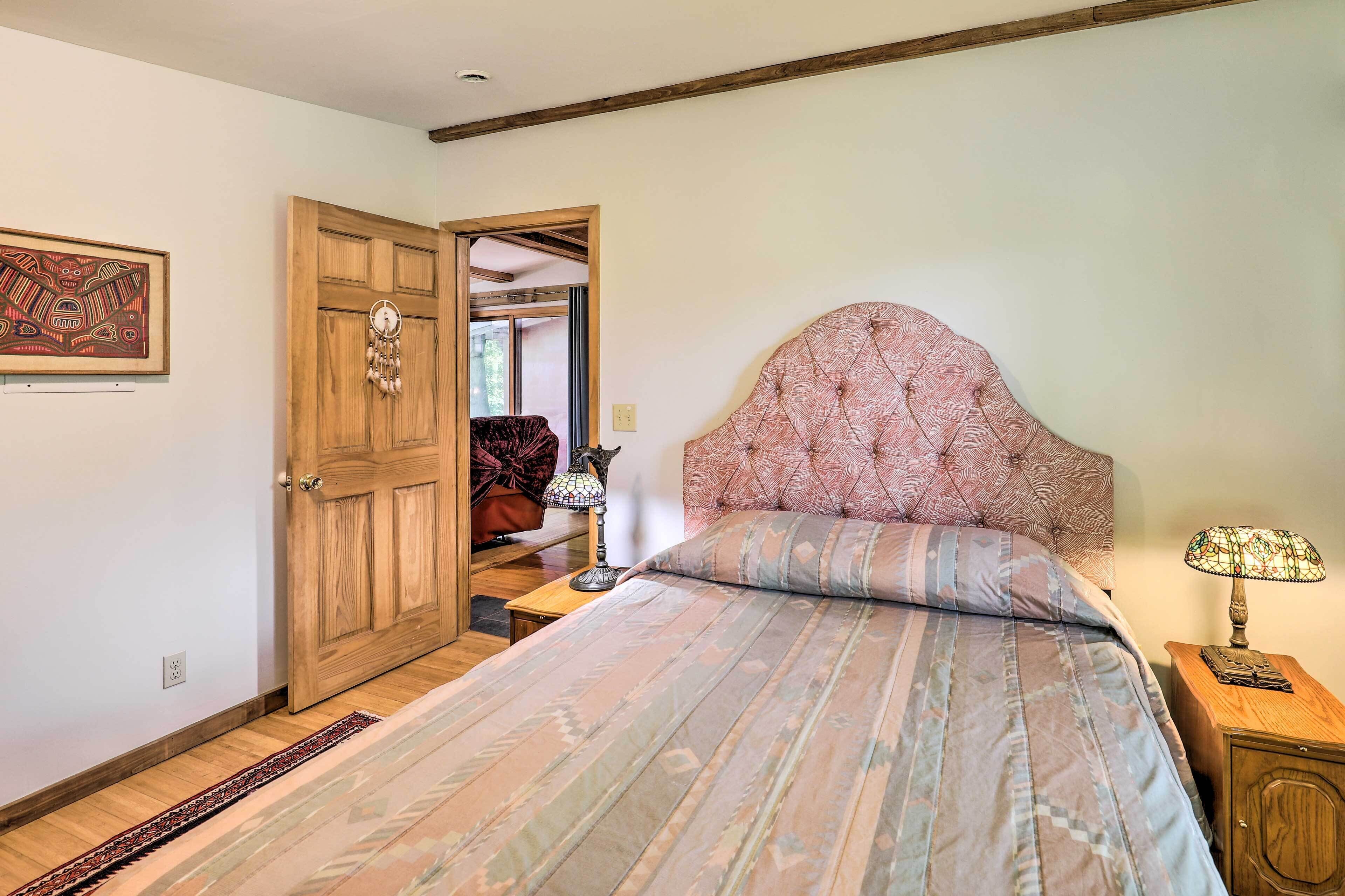 Une chambre à coucher avec un grand lit, une porte en bois, une petite table avec une lampe et un tableau encadré au mur.