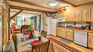 Une cuisine rustique avec des poutres en bois, un coin repas avec une table dressée pour deux personnes, et un espace de vie chaleureux avec un canapé et une plante.