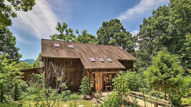 Un chalet en bois rustique, doté d’une véranda, entouré d’une végétation luxuriante et d’arbres.