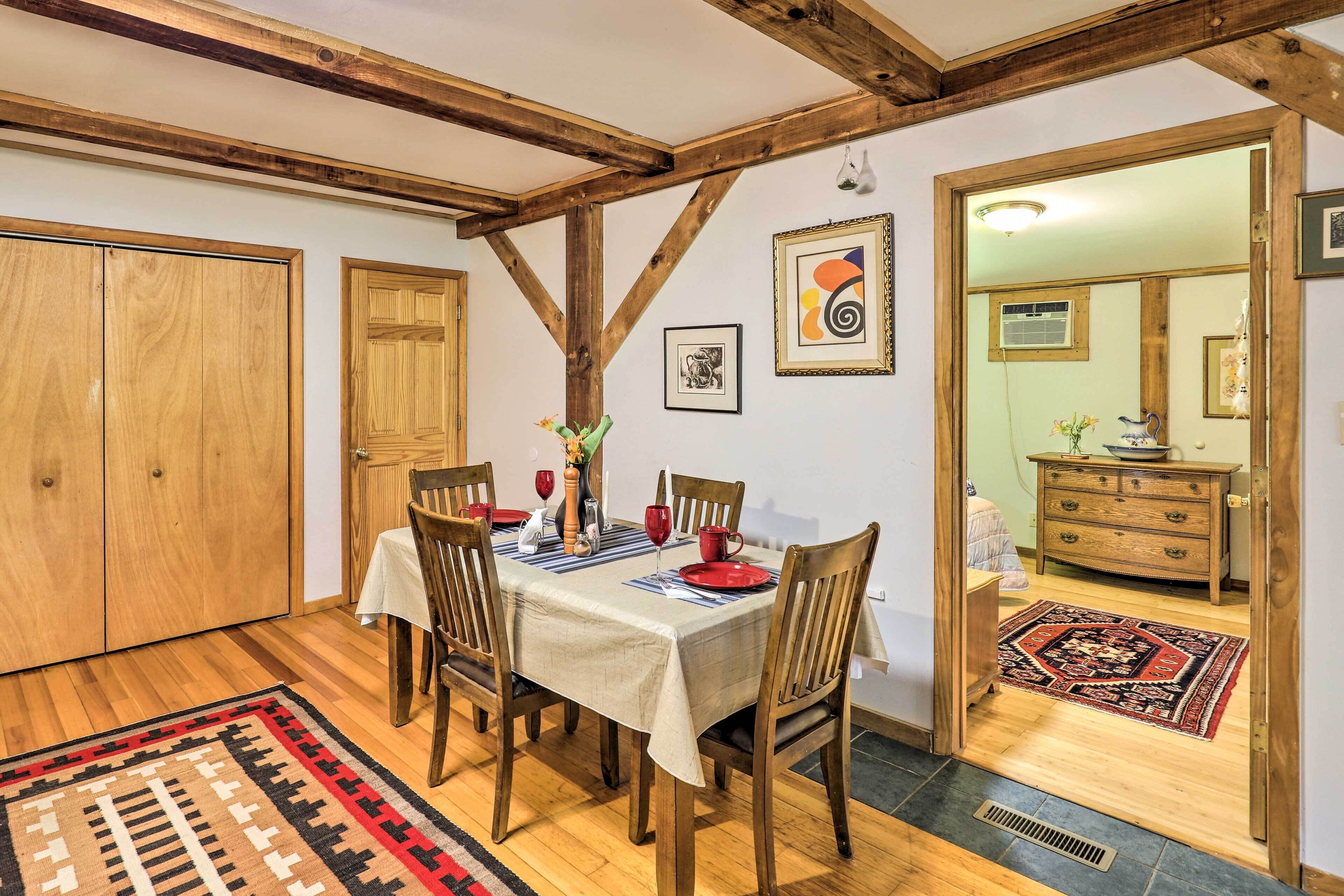A dining area with wooden chairs and a table set for four, a wooden ceiling with exposed beams, and a patterned rug on the floor.
