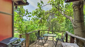 Une terrasse en bois équipée d’un barbecue, de deux chaises et d’une table, offrant une vue sur un paysage verdoyant et luxuriant.