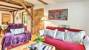 Un salon chaleureux avec un plafond en bois, un canapé rouge, un fauteuil violet et une table basse sur laquelle est posé un vase de fleurs.