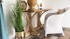 Ein Zimmer mit einem Holztisch, einem weißen Korbstuhl und einem Blumentopf.