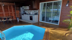 Eine Holzterrasse mit Swimmingpool, Essbereich und Küche.