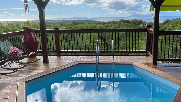 Eine Holzterrasse mit Swimmingpool, Schaukelstuhl und roter Vase.