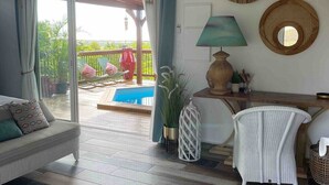 Ein Zimmer mit einer Schiebeglastür, die auf einen Balkon mit Pool führt, einer Couch, einem Tisch mit Lampe und dekorativer Wandkunst.