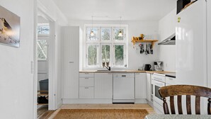 Une cuisine avec des meubles blancs, une fenêtre donnant sur des arbres, un plan de travail en bois et un luminaire suspendu.