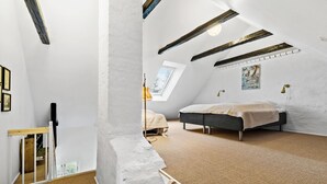 Une chambre avec un plafond en pente, un lit, une fenêtre et un tableau accroché au mur.