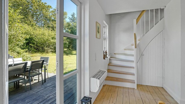 Un intérieur moderne avec un escalier en bois, un coin repas doté de sièges extérieurs et de grandes fenêtres offrant une vue sur l’extérieur.