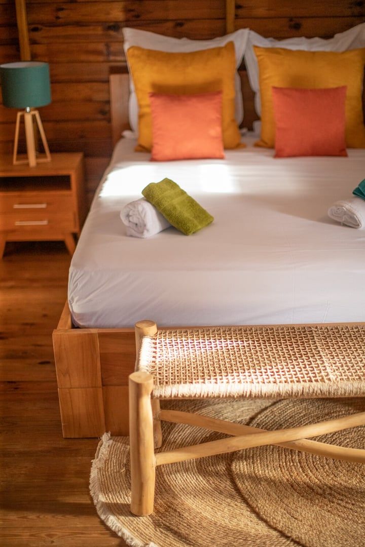 Un lit en bois avec une literie blanche, des coussins colorés et une serviette enroulée.