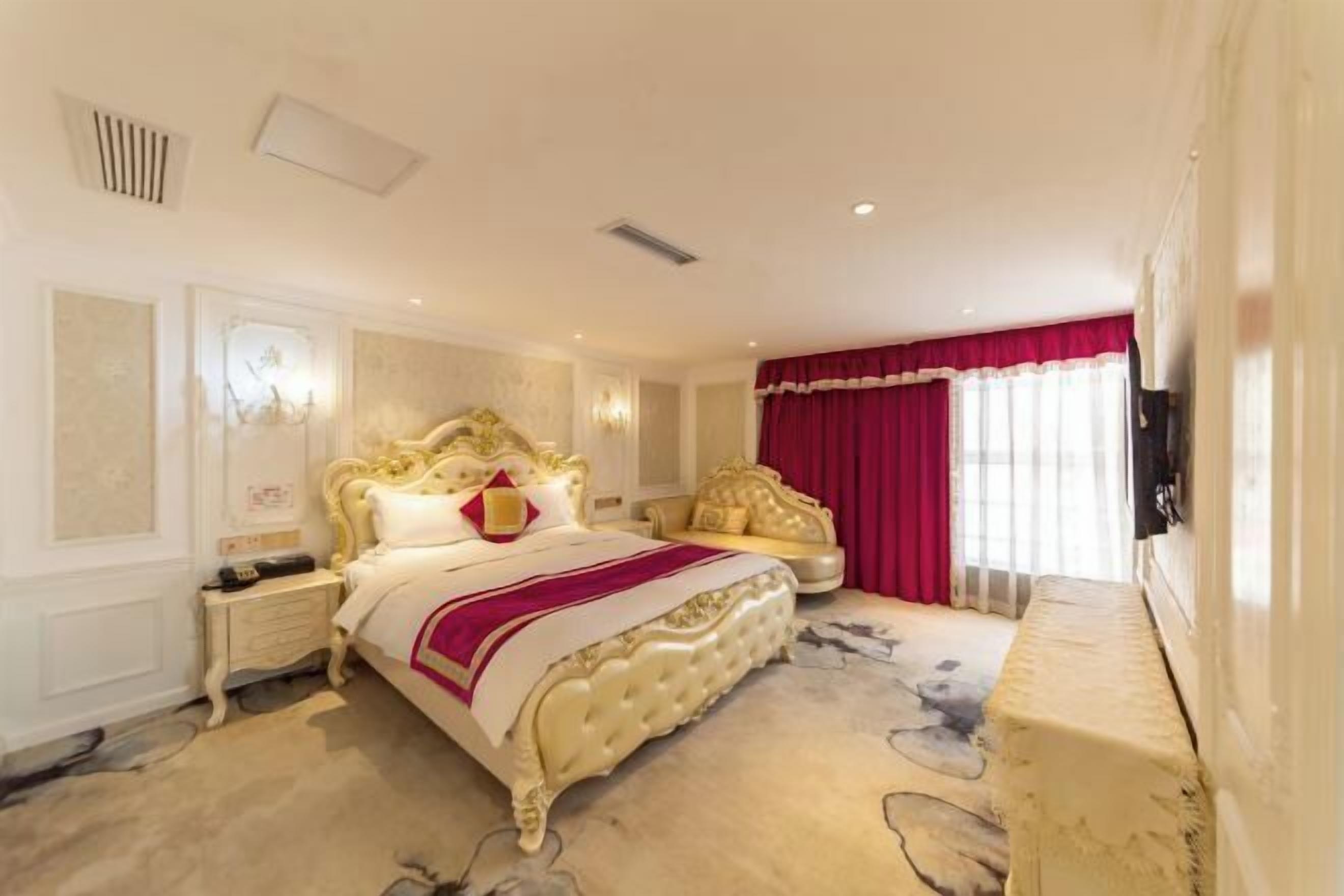 Une chambre à coucher luxueuse, avec un lit somptueux, un rideau rouge et un téléviseur fixé au mur.