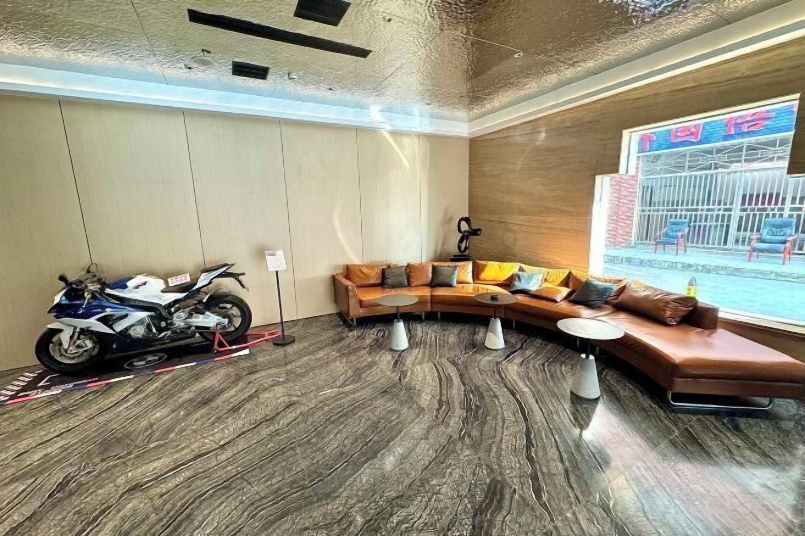 A modern interior with a curved sofa, a motorcycle, and a view of a building outside.