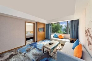 A modern hotel room with a large window, a sofa with colorful cushions, a small table, and a bed with a wooden headboard. - Shangpin Mijiang Hotel (Yanting)
