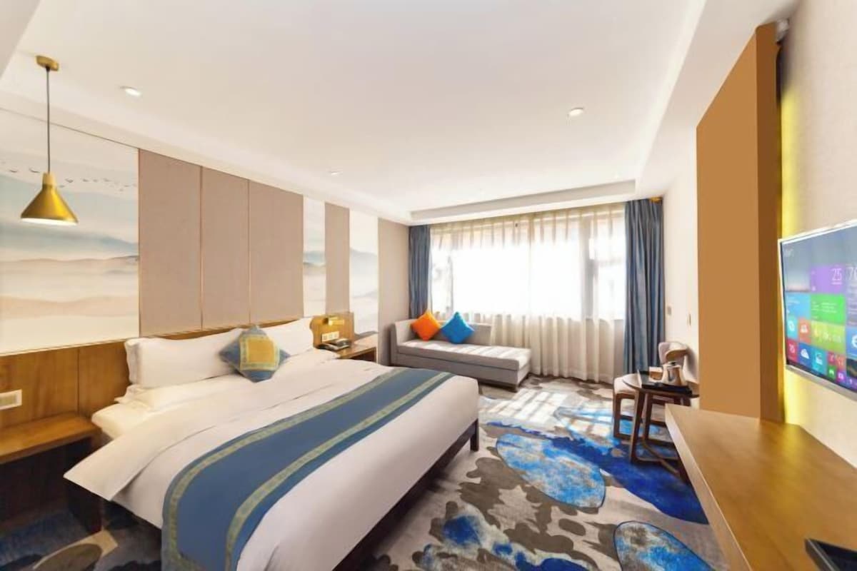 A hotel room with a bed, a seating area, a TV, and a large window.