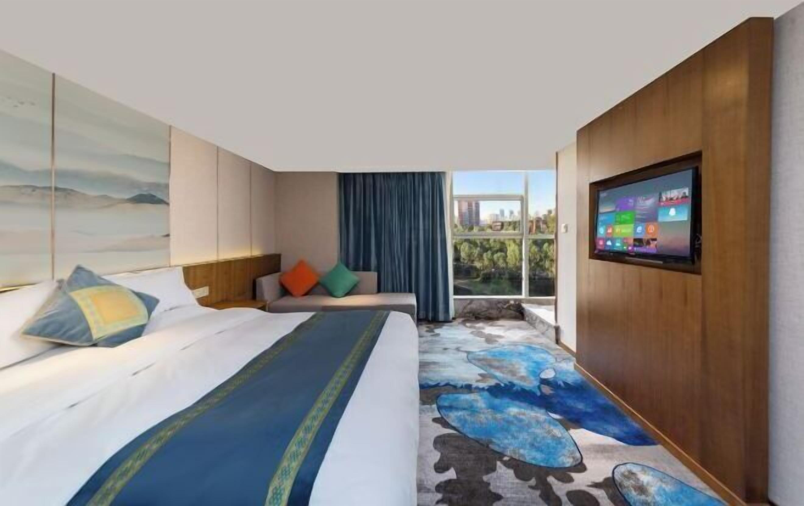 A modern hotel room with a large bed, a sofa, a TV, and a view of the city.