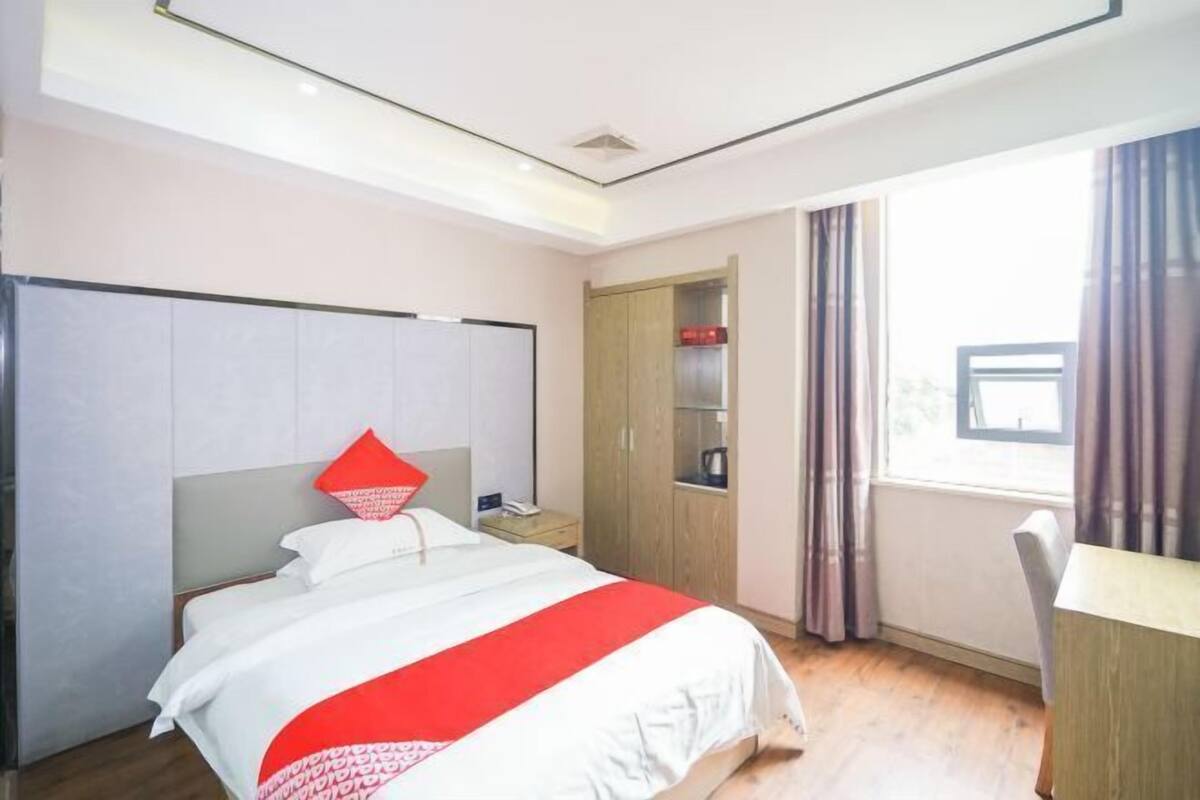 Une chambre d’hôtel avec un lit, une armoire, un bureau et une fenêtre avec des rideaux.