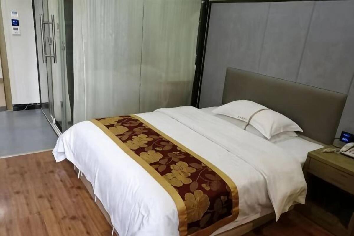 Une chambre d’hôtel avec un lit, une table de chevet, une commode, une porte vitrée et un plancher en bois.