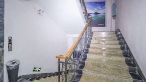 Eine Treppe mit Handlauf, einem Mülleimer, einem Notausgangsschild und einer Wandleuchte.