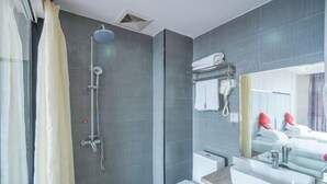Ein modernes Badezimmer mit Dusche, Toilette, Waschbecken und einem Spiegel, der ein Bett mit roten Kissen reflektiert.