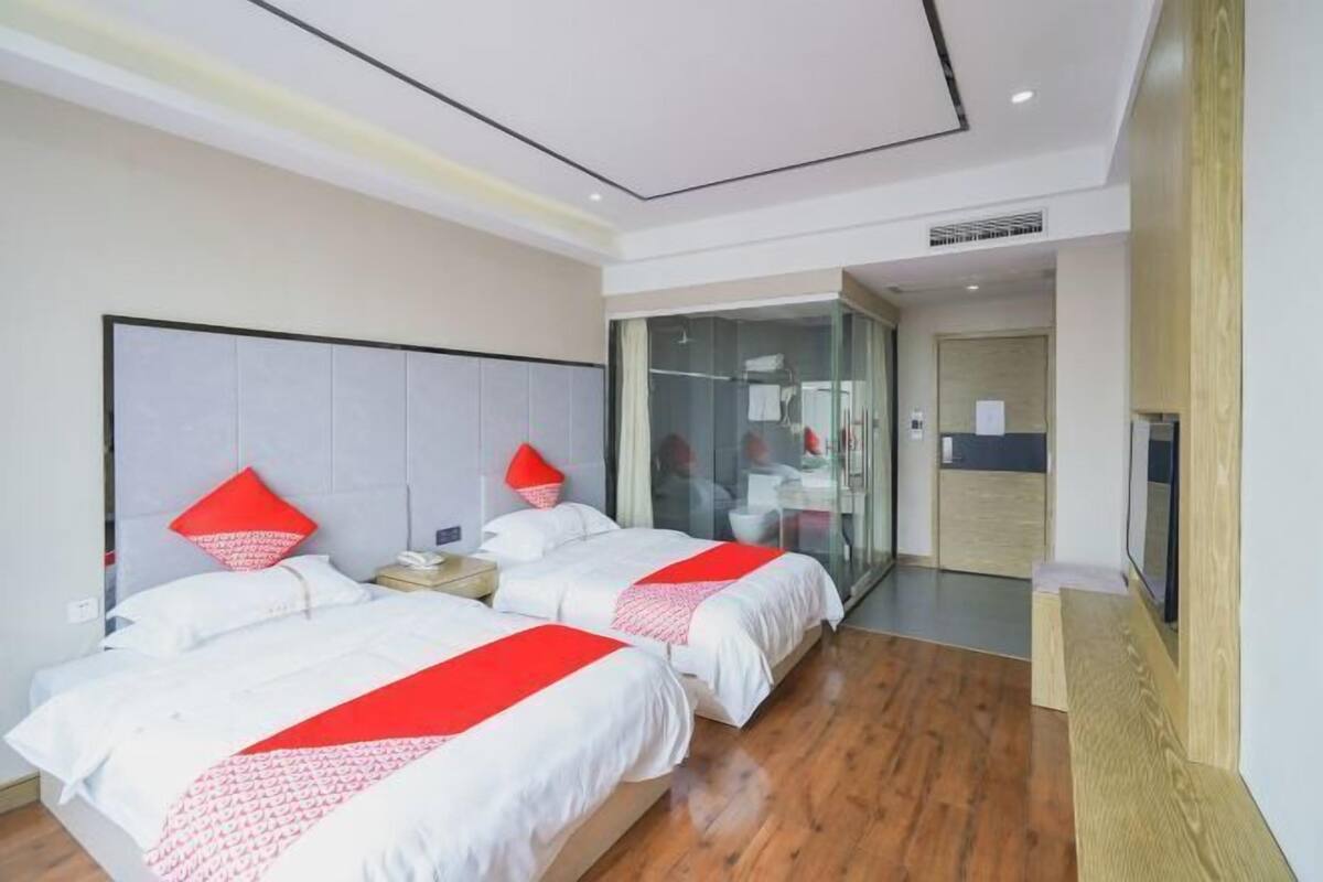 Une chambre d’hôtel avec deux lits, une télévision, une douche en verre et un plancher en bois.