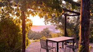 Un patio al aire libre con mesa y sillas, rodeado de árboles y vistas a colinas.