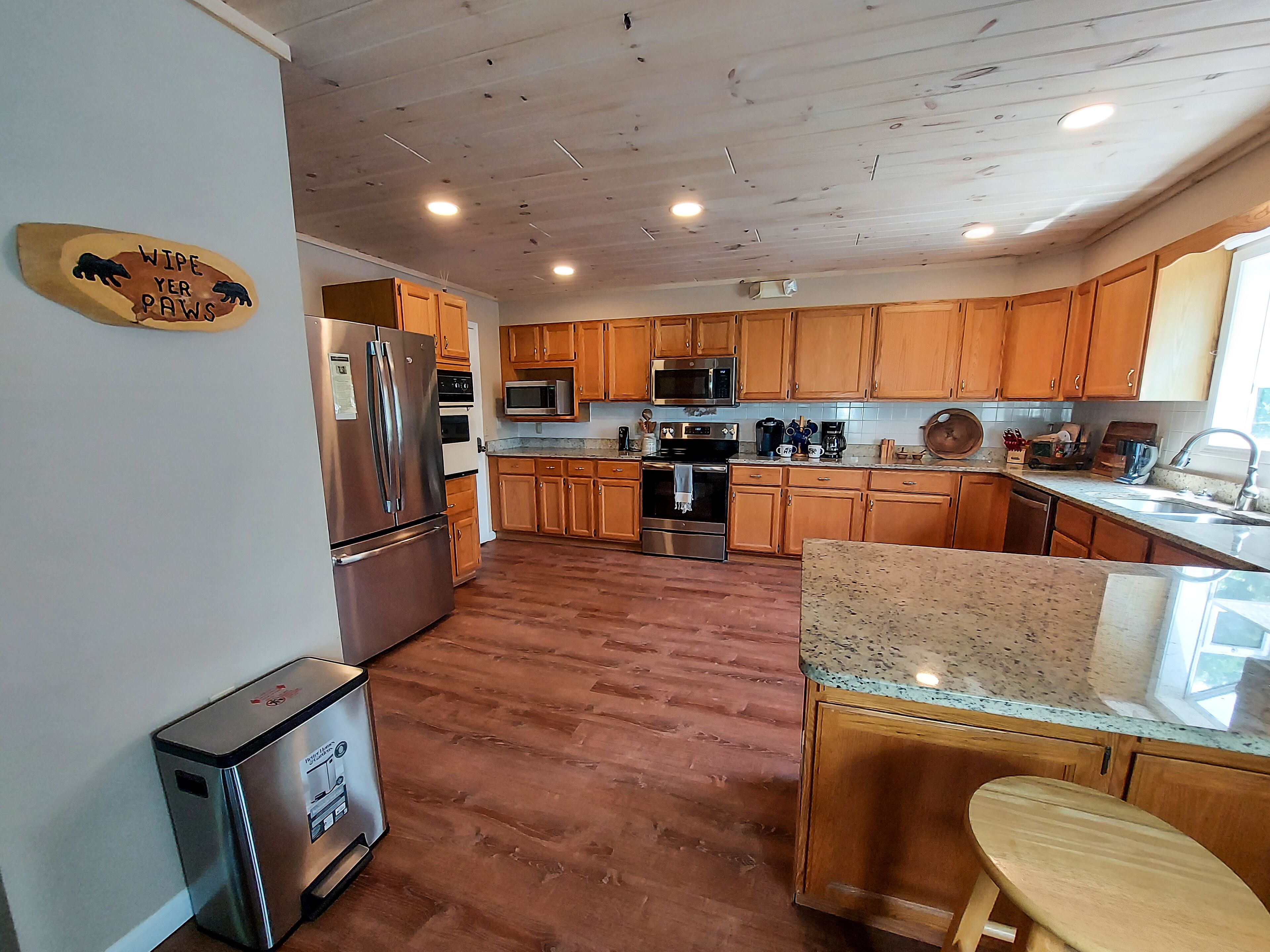 A kitchen with wooden cabinets, stainless steel appliances, a granite countertop, and a wooden stool.