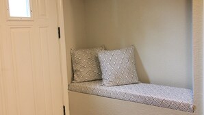 A hallway with a white door, a bench with patterned cushions, and storage baskets on shelves.
