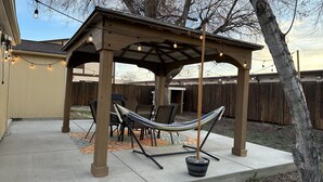 A covered patio area with a hammock, outdoor furniture, and string lights.
