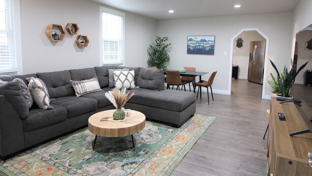 A modern living room with a grey sectional sofa, a wooden coffee table, and a dining area with a table and chairs.