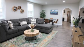 A modern living room with a grey sectional sofa, a wooden coffee table, and a dining area with a table and chairs. - 20 min to RedRocks, 15 min to downtown, 420ok, Free RV parking, Private, dogs ok (Arvada)